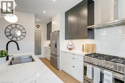 Kitchen featuring tasteful backsplash, wall chimney range hood, light wood-style floors, stainless steel appliances, and a sink - 