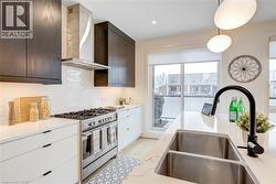 Kitchen featuring high end stove, dark brown cabinetry, wall chimney range hood, a sink, and decorative backsplash - 