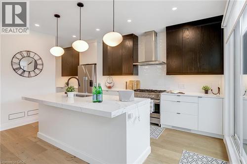 Kitchen featuring light wood-type flooring, wall chimney exhaust hood, dark brown cabinets, and appliances with stainless steel finishes - 151C Port Robinson Road, Pelham, ON - Indoor Photo Showing Kitchen With Upgraded Kitchen
