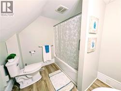Bathroom featuring wood finished floors, shower / bath combination with curtain, and vaulted ceiling - 