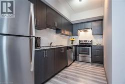 Kitchen featuring appliances with stainless steel finishes, under cabinet range hood, light wood finished floors, tasteful backsplash, and light stone counters - 