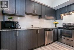 Kitchen with stainless steel appliances, a sink, under cabinet range hood, light wood-type flooring, and light stone counters - 