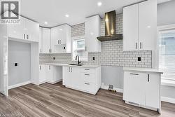 Kitchen with white cabinetry, wall chimney range hood, tasteful backsplash, light wood finished floors, and recessed lighting - 
