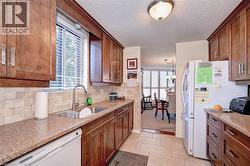 Kitchen with white appliances, a sink, tasteful backsplash, a textured ceiling, and light tile patterned floors - 