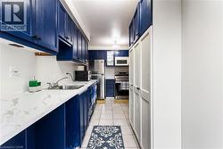 Kitchen with blue cabinets, stainless steel appliances, light tile patterned flooring, backsplash, and light stone counters - 