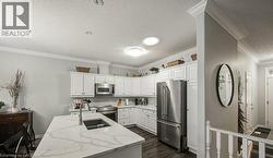 Kitchen featuring appliances with stainless steel finishes, white cabinetry, dark wood finished floors, a center island with sink, and ornamental molding - 