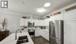 Kitchen featuring premium appliances, ornamental molding, white cabinets, light stone countertops, and dark wood finished floors - 