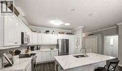 Kitchen with appliances with stainless steel finishes, white cabinets, light stone countertops, a kitchen breakfast bar, and crown molding - 