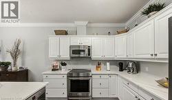 Kitchen with stainless steel appliances, white cabinetry, ornamental molding, light stone counters, and a textured ceiling - 