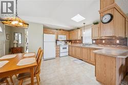 Kitchen with white appliances, a skylight, light countertops, pendant lighting, and a peninsula - 