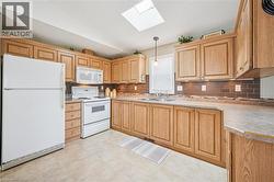Kitchen with white appliances, backsplash, light countertops, light brown cabinetry, and pendant lighting - 