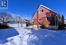 View of snowy exterior featuring a chimney, brick siding, an outbuilding, and a detached garage - 