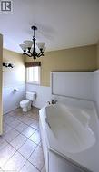 Bathroom featuring wainscoting, a bath, a textured ceiling, light tile patterned floors, and a chandelier - 