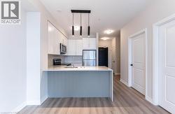 Kitchen featuring a peninsula, white cabinetry, appliances with stainless steel finishes, decorative light fixtures, and light wood-style flooring - 