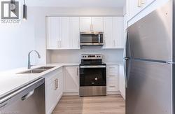 Kitchen with stainless steel appliances, white cabinetry, and light wood finished floors - 