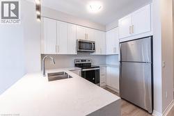 Kitchen with stainless steel appliances, light stone countertops, white cabinets, and light wood-type flooring - 