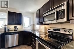 Kitchen with appliances with stainless steel finishes, tasteful backsplash, dark cabinets, light tile patterned floors, and a textured ceiling - 
