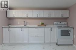 Kitchen with white range with electric stovetop, white cabinetry, and light marble finish floors - 