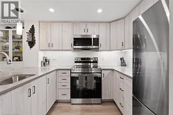 Kitchen featuring stainless steel appliances, tasteful backsplash, light stone counters, decorative light fixtures, and light wood finished floors - 