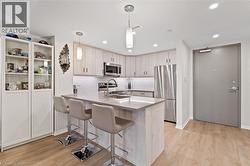 Kitchen with a peninsula, stainless steel appliances, a kitchen breakfast bar, decorative light fixtures, and light wood-type flooring - 