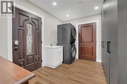Laundry area featuring stacked washer / dryer, light wood finished floors, recessed lighting, and cabinet space - 