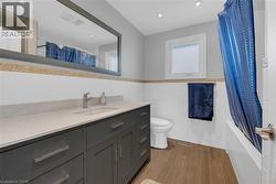 Full bathroom with tile walls, dark wood finished floors, shower / tub combo with curtain, vanity, and a wainscoted wall - 