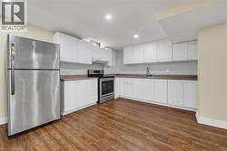 Kitchen with stainless steel appliances, white cabinetry, recessed lighting, dark wood-style floors, and under cabinet range hood - 