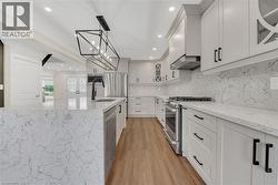 Kitchen featuring glass insert cabinets, light stone counters, stainless steel appliances, pendant lighting, and a large island - 