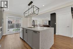 Kitchen with hanging light fixtures, a center island with sink, ornamental molding, light stone counters, and light wood-style floors - 