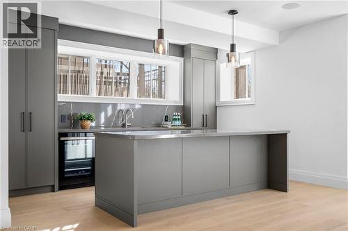 Indoor wet bar with gray cabinetry, light wood-style flooring, tasteful backsplash, wine cooler, and pendant lighting - 1322 Minaki Road, Mississauga, ON - Indoor Photo Showing Kitchen