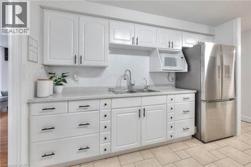 Kitchen featuring white cabinetry, light countertops, backsplash, microwave - 35 Green Valley Drive Unit# 103, Kitchener, ON - Indoor Photo Showing Kitchen With Double Sink