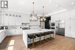 Kitchen featuring a breakfast bar, appliances with stainless steel finishes, light stone counters, white cabinetry, and recessed lighting - 