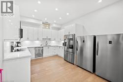 Kitchen featuring white cabinets, appliances with stainless steel finishes, light stone counters, decorative backsplash, and light wood finished floors - 