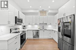 Kitchen with stainless steel appliances, white cabinets, decorative backsplash, light wood-style flooring, and recessed lighting - 