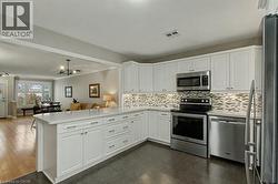 Kitchen with appliances with stainless steel finishes, white cabinets, open floor plan, a peninsula, and tasteful backsplash - 