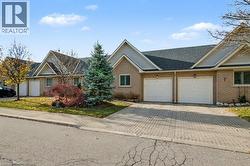 View of front of house featuring an attached garage, decorative driveway, brick siding, and roof with shingles - 