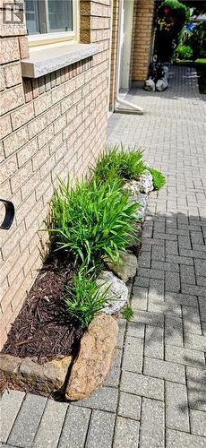 Brick exterior featuring a stone window sill, a rock-lined garden bed with green foliage, and a paver pathway - 165 Main Street E Unit# 9, Grimsby, ON - Outdoor