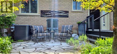 Expansive flagstone patio with surrounding foliage, brick exterior, and a black-railed deck with stairs - 165 Main Street E Unit# 9, Grimsby, ON - Outdoor With Deck Patio Veranda