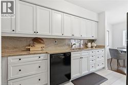 Kitchen with white cabinets, light stone counters, black dishwasher, and decorative backsplash - 