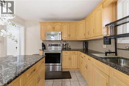 Kitchen featuring stainless steel appliances, hanging light fixtures, dark stone countertops, backsplash, and light brown cabinetry - 364 Roselawn Place, Waterloo, ON - Indoor Photo Showing Kitchen
