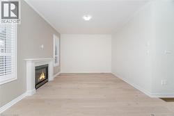 Unfurnished living room featuring a glass covered fireplace, light wood finished floors, and crown molding - 