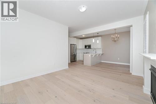 Unfurnished living room featuring a chandelier, light wood finished floors, and a fireplace - 28 Pickett Place, Cambridge, ON - Indoor Photo Showing Kitchen