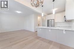 Kitchen featuring tasteful backsplash, light stone countertops, a peninsula, white cabinets, and stainless steel appliances - 