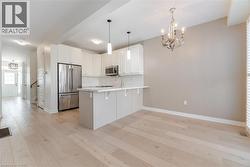 Kitchen with light wood-type flooring, hanging light fixtures, backsplash, white cabinets, and stainless steel appliances - 