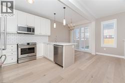 Kitchen with appliances with stainless steel finishes, tasteful backsplash, white cabinetry, a peninsula, and decorative light fixtures - 