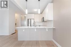 Kitchen with decorative backsplash, light wood finished floors, white cabinets, a breakfast bar area, and pendant lighting - 