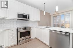 Kitchen with appliances with stainless steel finishes, light stone countertops, decorative light fixtures, and white cabinetry - 