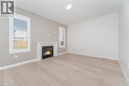 Unfurnished living room with healthy amount of natural light, light wood-style floors, and a glass covered fireplace - 28 Pickett Place, Cambridge, ON - Indoor Photo Showing Other Room With Fireplace