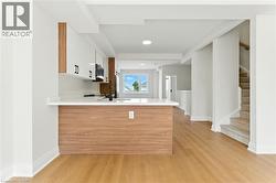 Kitchen featuring light wood-type flooring, white cabinetry, a peninsula, light stone counters, and modern cabinets - 