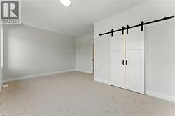 Unfurnished bedroom featuring a barn door, light carpet, and a closet - 